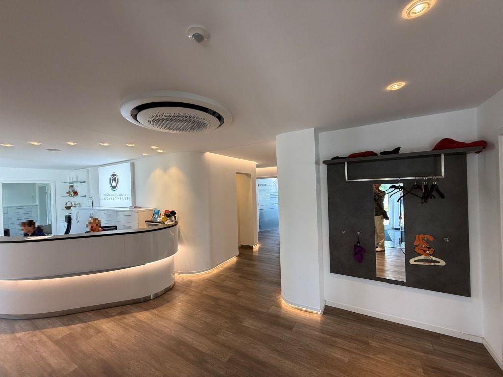 Hochwertig gestalteter Empfangsbereich mit indirekter Beleuchtung im Tresen. Lichtakzente an Decke und Sockel schaffen ein behagliches Ambiente. Die großzügige Garderobe unterstreicht das durchdachte Raumkonzept.